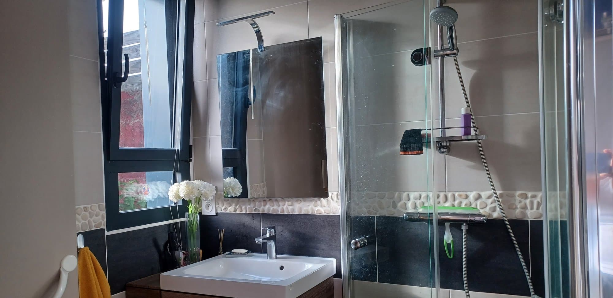 Salle d'eau de Quiétude à Brest, douche, vasque et frise en galets pour se rafraîchir avant ou après le soin.
